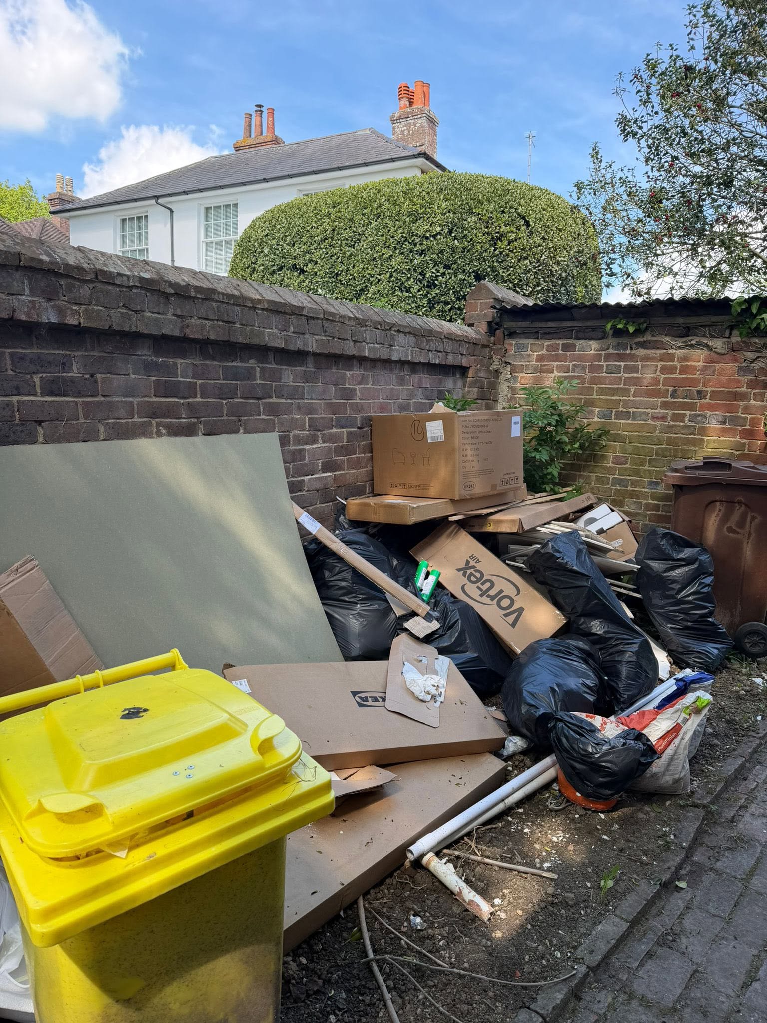 A rear garden area piled with cardboard, bin bags and rubbish before clearance